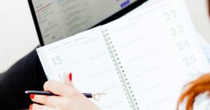 Woman using laptop and notebook for work organization and schedule planning indoors.